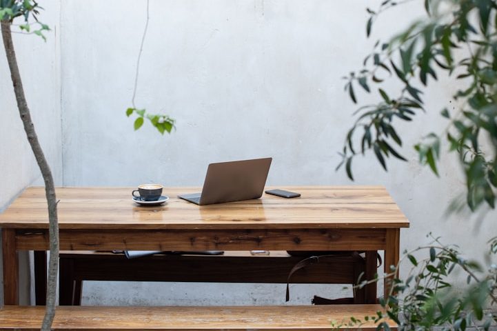 Leistungen für Selbstständige Laptop Kaffeetasse und Smartphone auf einem Holztisch in einem schlichten Innenhof